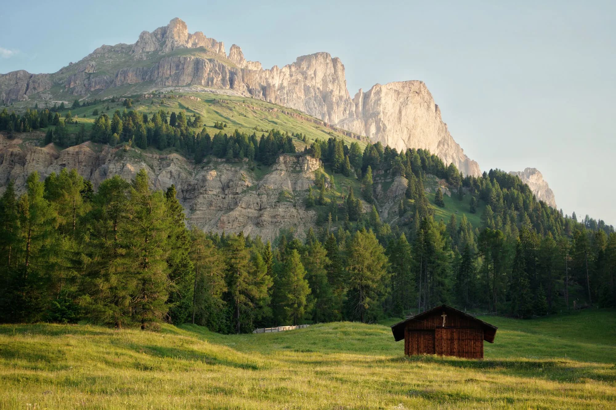 A small wooden cabin below sunlit Dolomites peaks